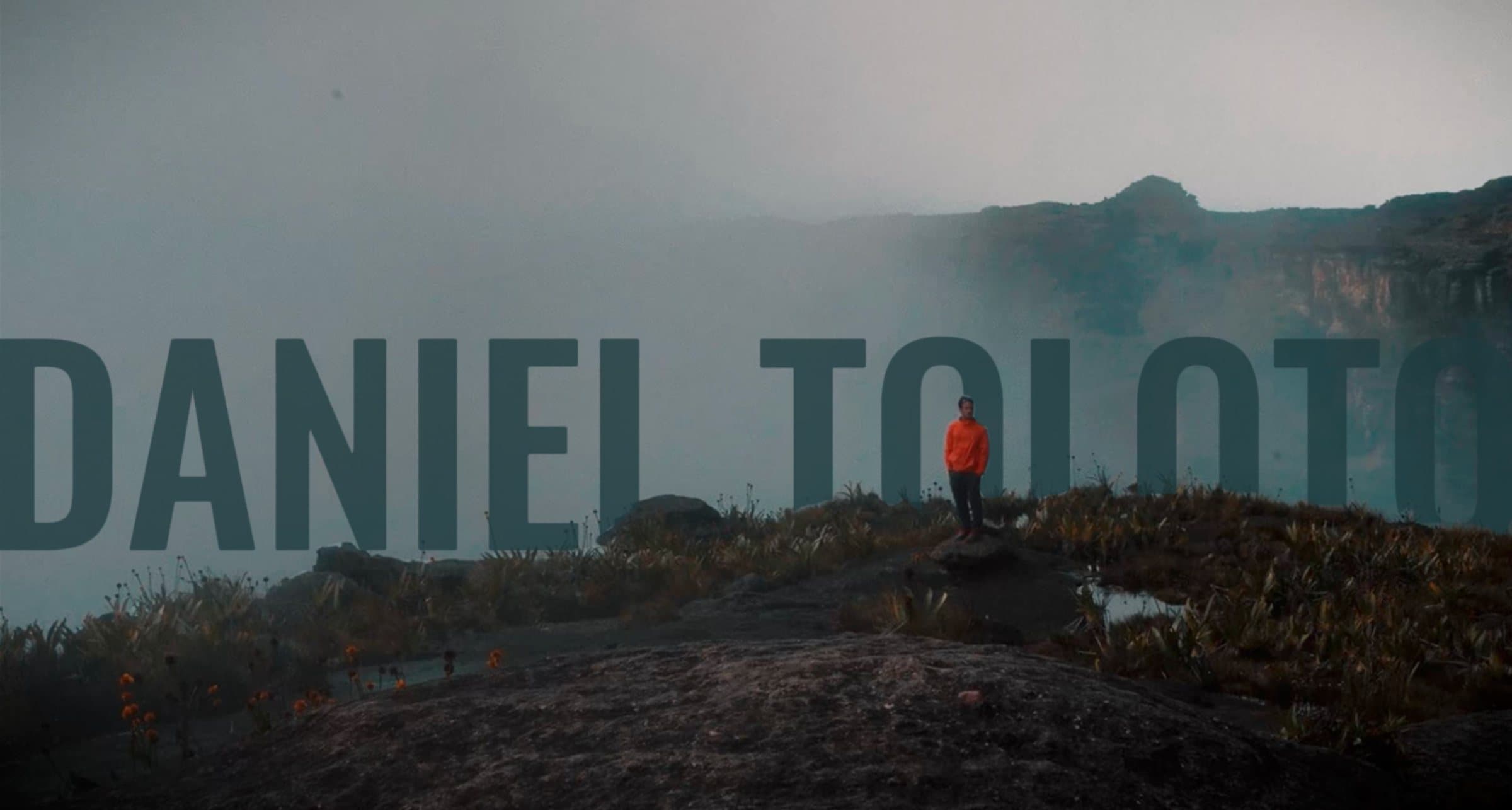 Daniel Toloto no alto de uma montanha, com o nome em letras grandes ao fundo